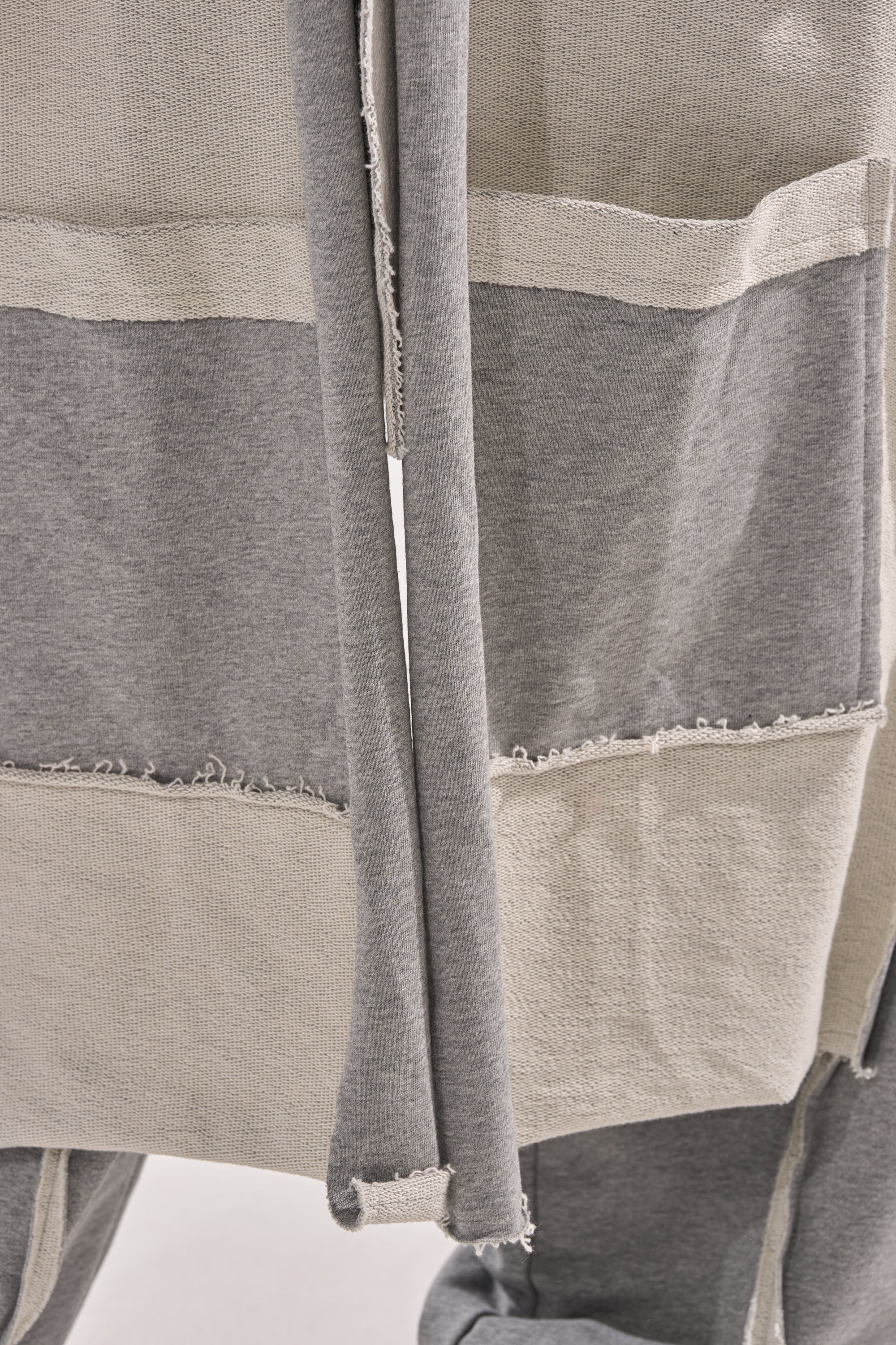 Close-up of gray and off-white color-blocked fabric with raw, frayed seams and textured panels—details from the IM UP NEXT DUSTER. Two fabric strips hang down the center of this casual, two-tone duster.