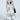 A person confidently poses in a fashionable two-tone patchwork outfit, featuring our IM UP NEXT DUSTER—a sleeveless hoodie with a plunging neckline—paired with wide-leg pants and sunglasses, accessorized with a black handbag and chunky necklace.