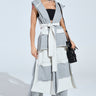 A person confidently poses in a fashionable two-tone patchwork outfit, featuring our IM UP NEXT DUSTER—a sleeveless hoodie with a plunging neckline—paired with wide-leg pants and sunglasses, accessorized with a black handbag and chunky necklace.
