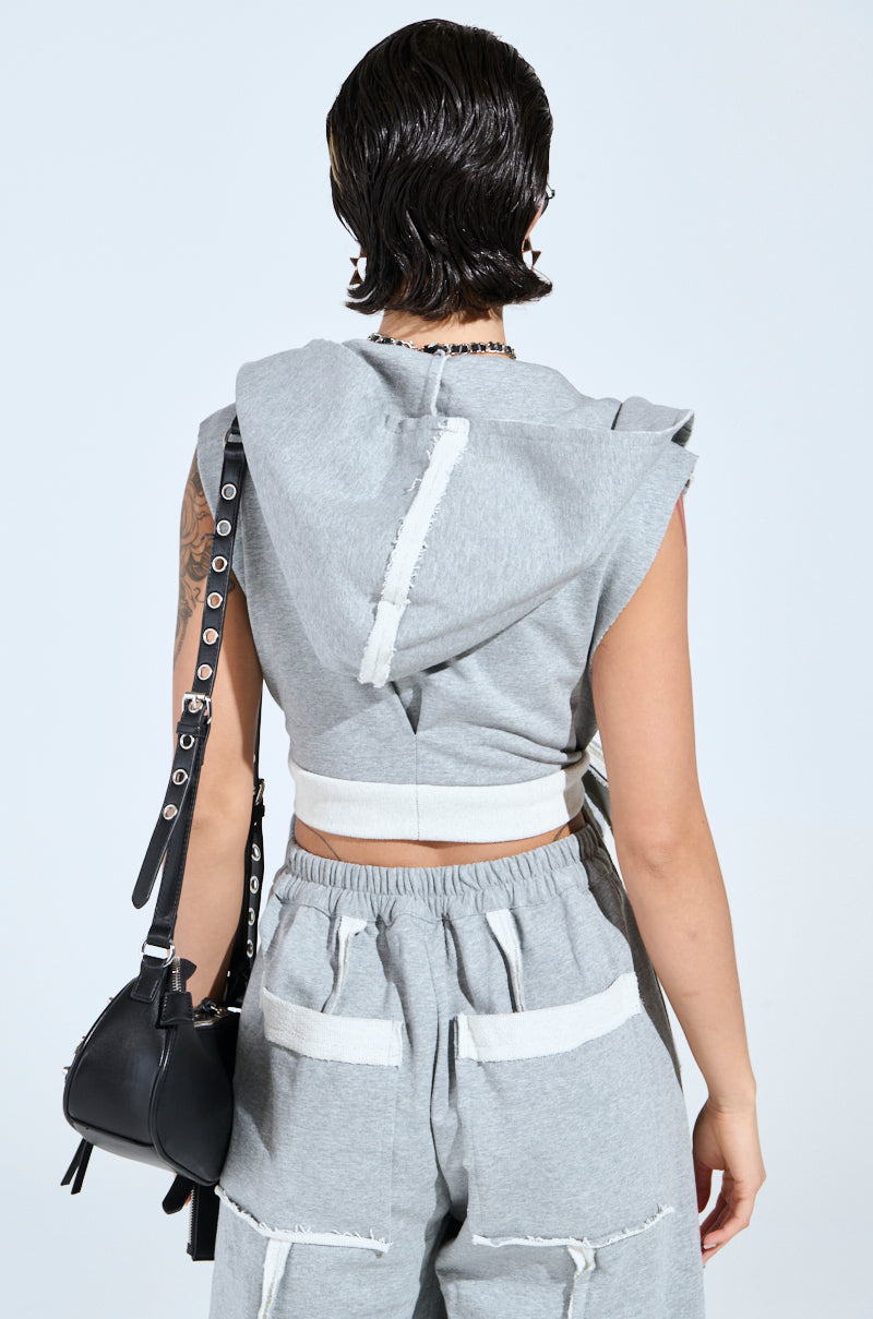 The back view of someone with short hair showcases them in a two-tone, sleeveless gray "IM UP NEXT DUSTER" hoodie and matching pants while carrying a small black strap bag against a plain white background.