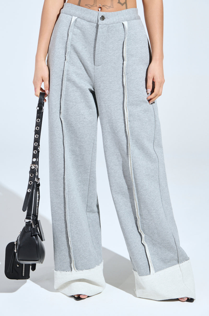 Someone is wearing IM UP NEXT TROUSER in gray with a high-rise, wide-leg fit, textured seaming, and white cuffs. They're holding a black handbag featuring a strap with metal studs and buckles. The background is plain and well-lit.