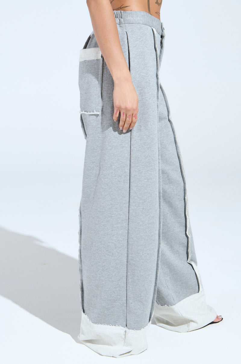 Wearing the IM UP NEXT TROUSER, someone poses against a plain backdrop. The gray pants have a high-rise fit, frayed edges, large pockets, a shirred elastic panel, and wide legs. Only their lower half is visible.