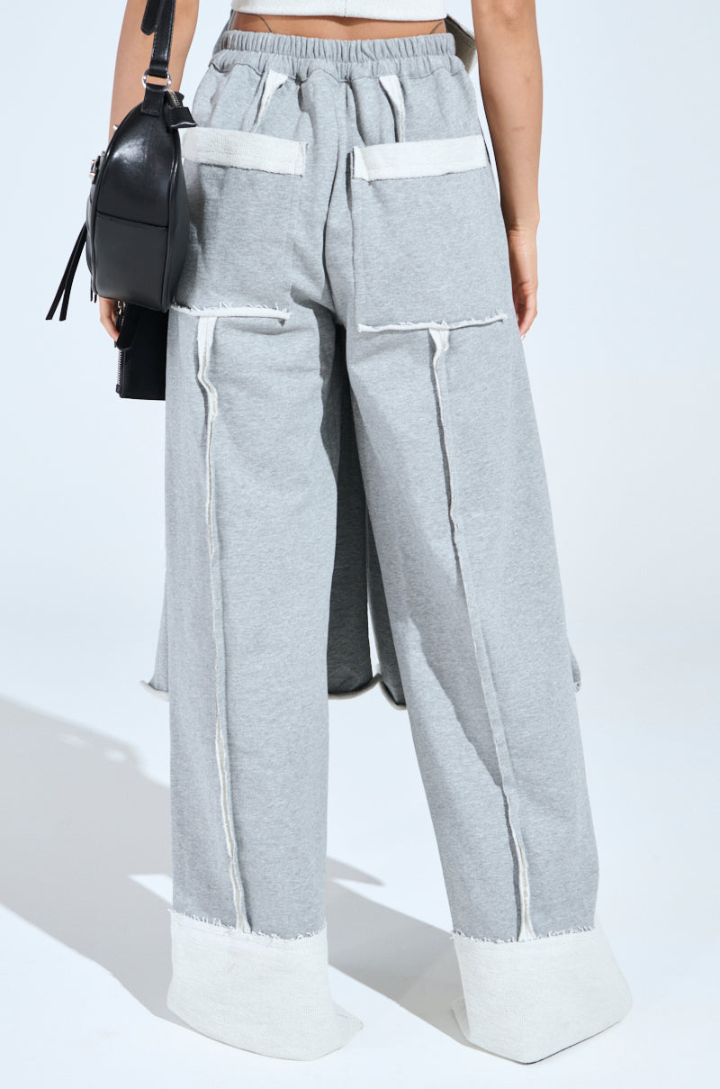 Back view of a person wearing the IM UP NEXT TROUSER, featuring loose-fitting gray pants with textured seaming, white trim at the high-rise waist with shirred elastic. They carry a small black bag on their shoulder set against a plain white background.