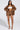 A woman poses confidently in a BIRDIE OVERSIZED BOMBER with a quilted interior, matching brown faux leather shorts, and a white tube top. Her hands rest on her hips while she stands against a plain backdrop in patterned shoes.