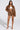 A person confidently models the BIRDIE OVERSIZED BOMBER with a quilted interior, paired with shorts and a white bandeau top, complemented by patterned heeled shoes. The backdrop is plain and light-colored.