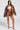 A woman confidently wears a BIRDIE OVERSIZED BOMBER with a quilted interior, perfectly paired with brown shorts and a white tube top. She completes her stylish look with high-heeled, pointed shoes against a light gray backdrop.