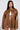 A person with long hair is wearing the BIRDIE OVERSIZED BOMBER, featuring a chic faux leather exterior and quilted interior. It's paired perfectly with matching shorts, hoop earrings, and a white top. The plain, light-colored backdrop accentuates their bold fashion statement.
