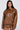 A person with long dark hair models the BIRDIE OVERSIZED BOMBER in brown faux leather. Featuring a front zipper, flap pockets, and a quilted interior for warmth, the jacket stands out against a plain white background, enhancing its stylish appeal.