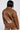 A person with long black hair wears a BIRDIE OVERSIZED BOMBER, featuring a shiny brown faux leather finish, a wide collar, and long sleeves. They are shown from the back against a plain, light-colored background.