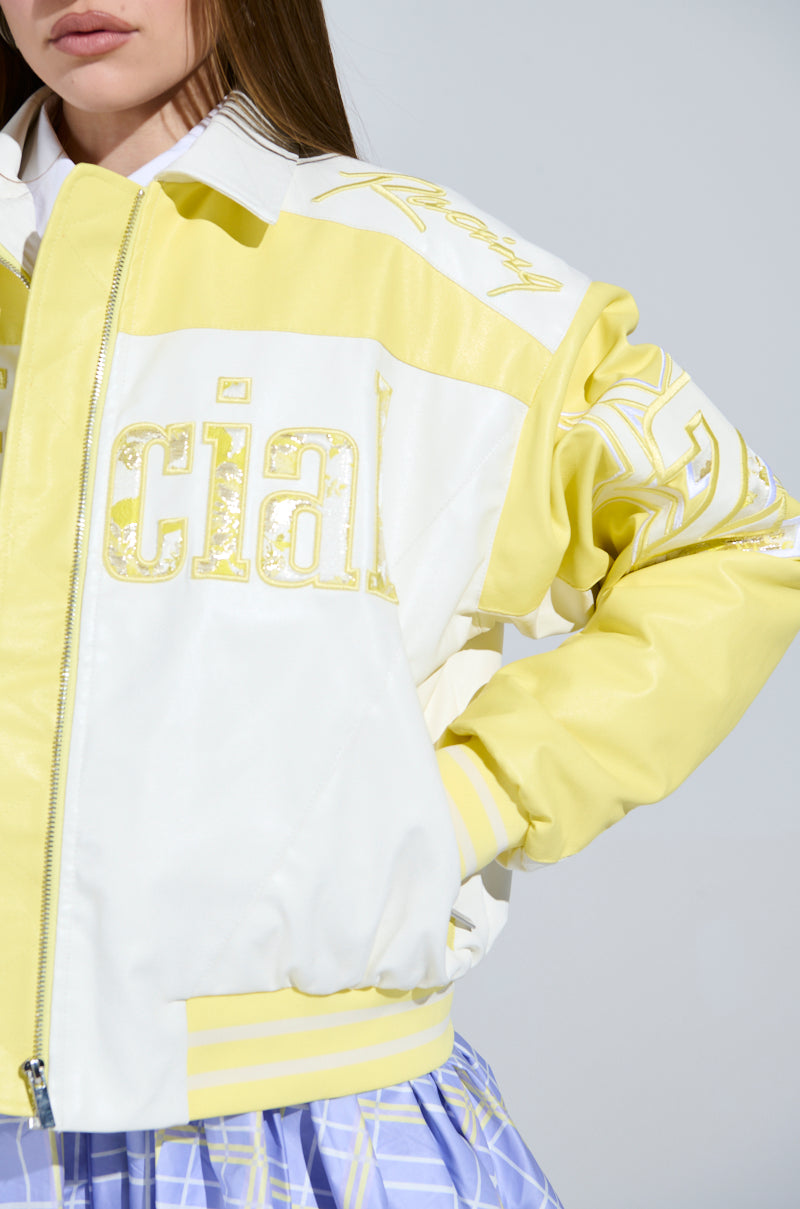 Someone is sporting the UNOFFICIAL RACER BOMBER in yellow and white with "social" on it, featuring a zip, striped cuffs, and faux leather accents. It's paired with a blue and white patterned skirt against a light gray backdrop.
