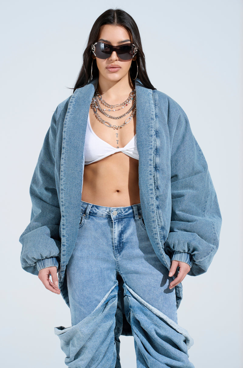 Wearing a LAY UP AND CHILL DENIM COCOON COAT and unique split knee jeans with a white top, long dark hair, sunglasses, and layered necklaces against a blue sky.