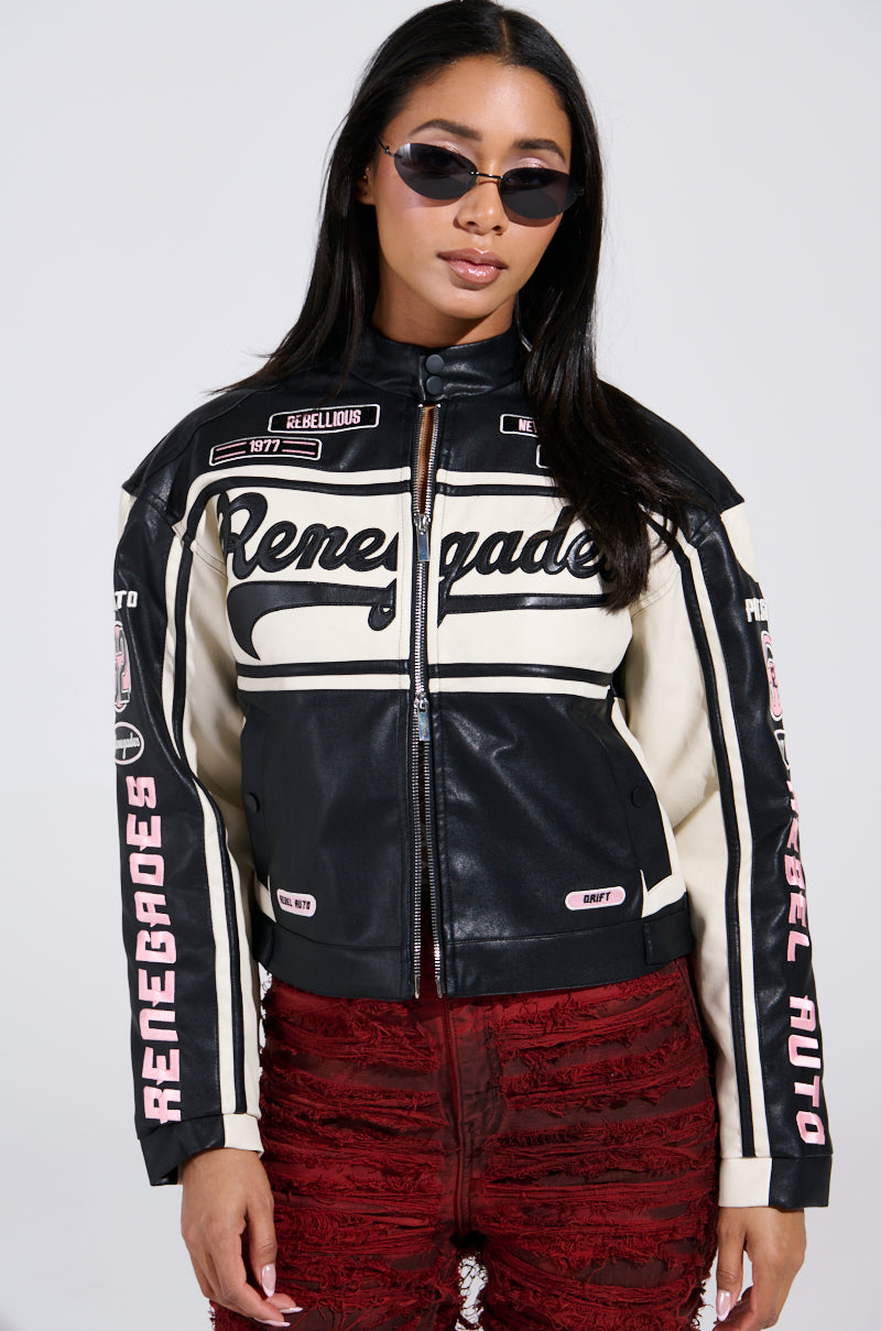 A woman poses against a plain background, hands in pockets, wearing the RENEGADES EMBROIDERED MOTO jacket with text and patches for a vintage, rebellious look, paired with red textured pants and sunglasses.