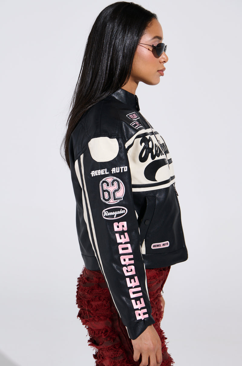 A person with long dark hair wearing sunglasses dons the RENEGADES EMBROIDERED MOTO jacket, featuring "62" and multiple patches. Paired with red textured pants, this ensemble stands out against a plain background for a striking color block effect.