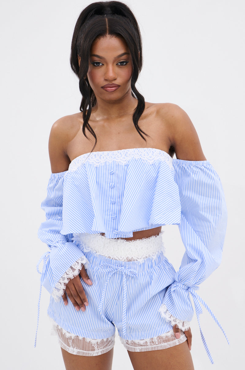 A woman models the PRAIRIE CHIC OFF THE SHOULDER LONG SLEEVE BLOUSE in blue and white with matching high-waisted shorts featuring white lace trim, against a plain white background.
