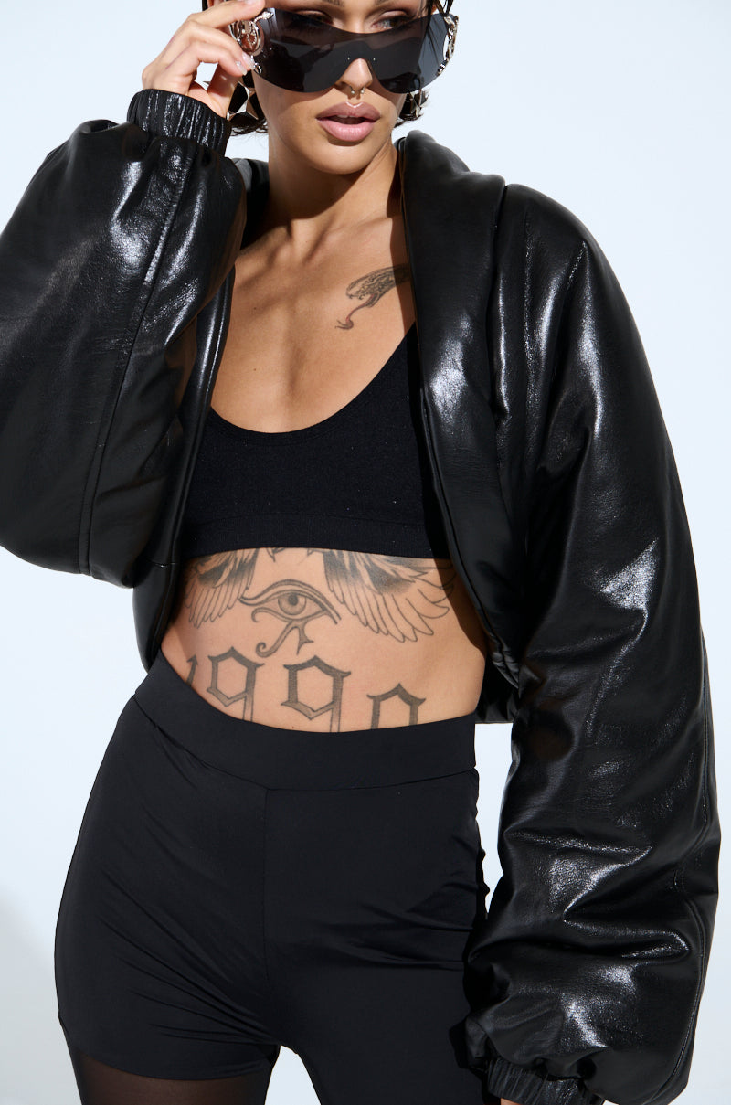 Wearing a BUTTER LUXE COCOON SHRUG, sleek black crop top, and high-waisted shorts, the person exudes effortless edginess. Sunglasses shield their eyes as tattoos—a striking eye and "1990"—are on display.