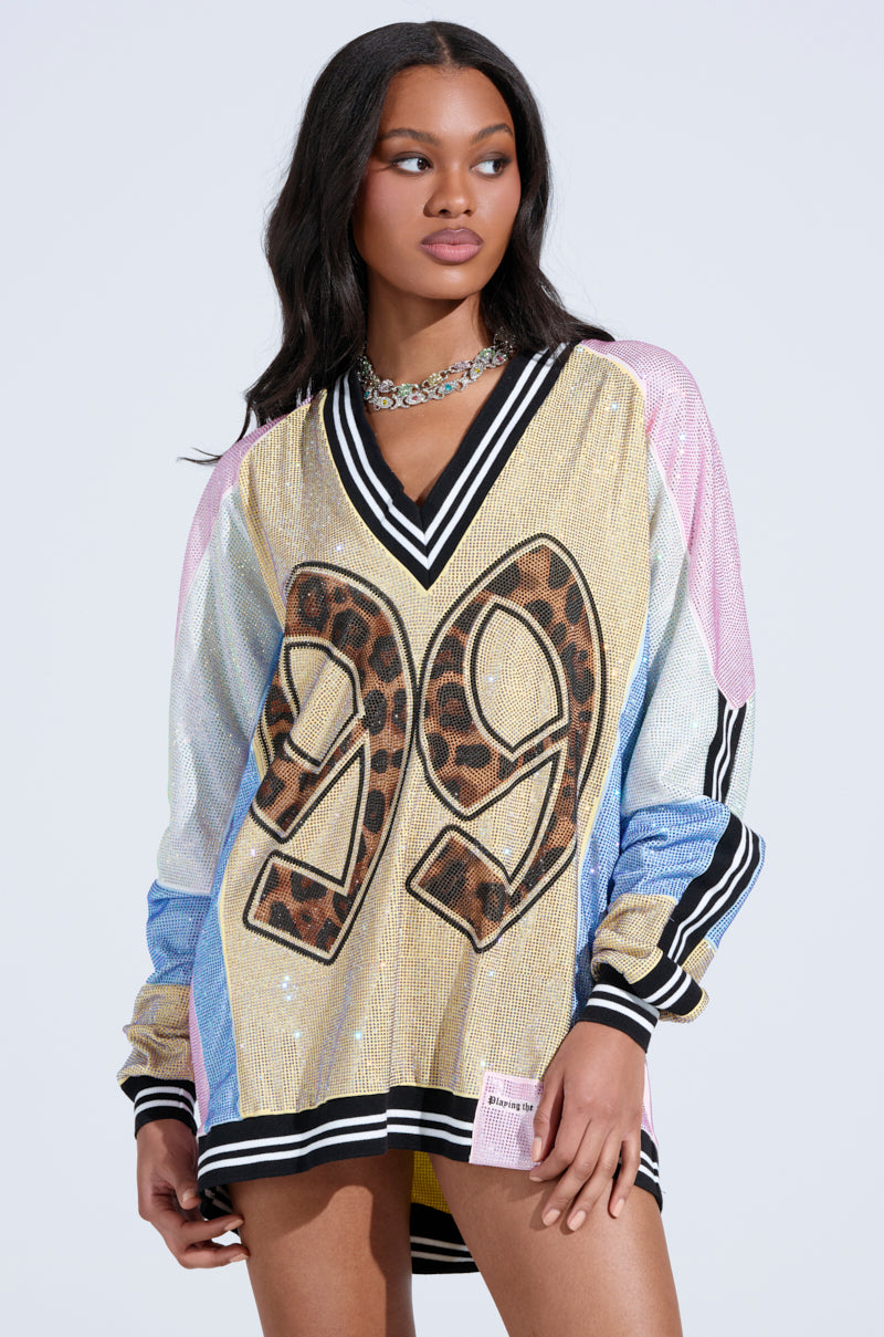 A woman models the RYAN Colorblock Rhinestone Jersey Mini Dress in pastel, featuring an oversized fit, sparkling rhinestones, leopard-print 99, multicolored sleeves, and black-and-white striped trim against a light background.