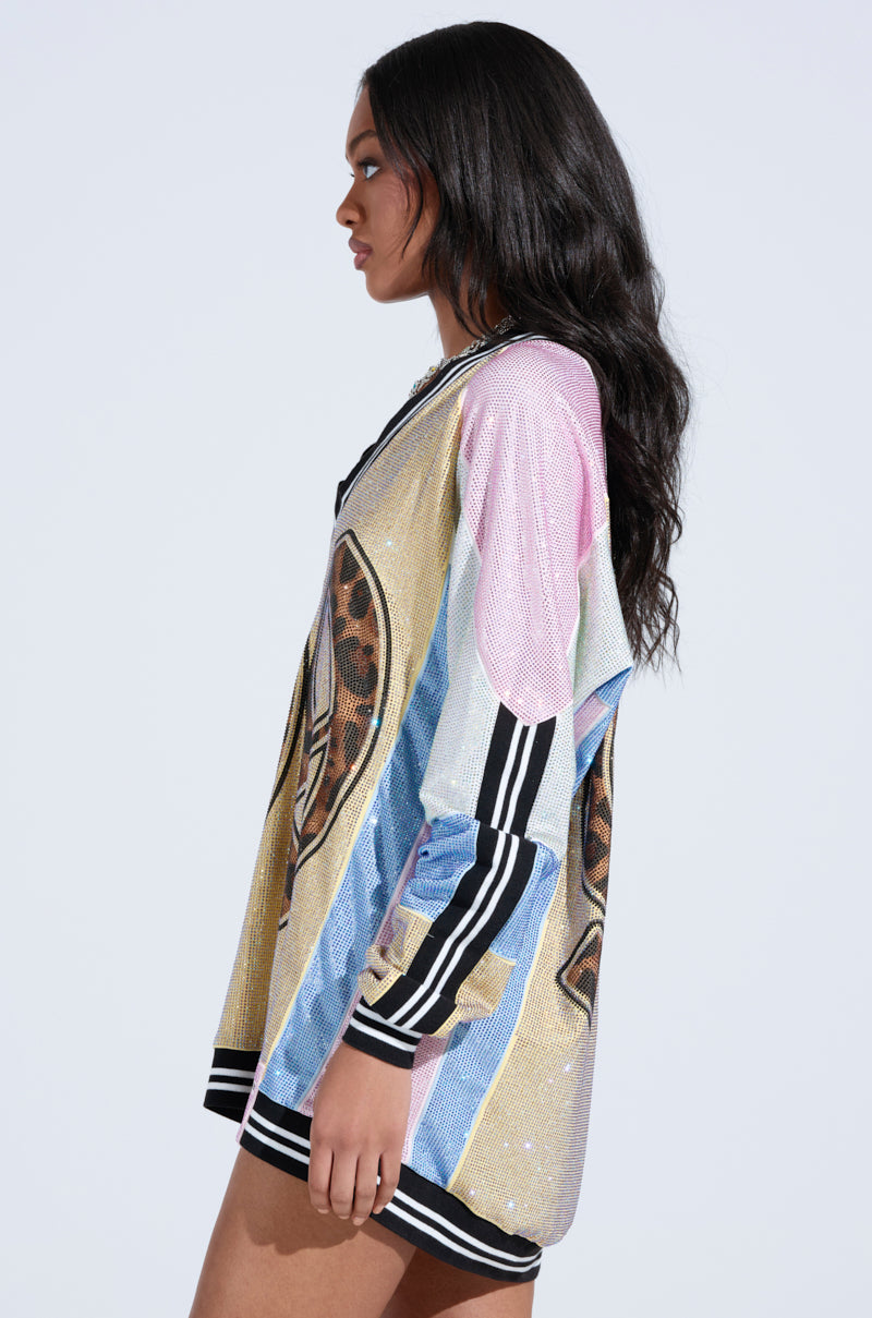 A woman with long wavy hair stands sideways in the RYAN Colorblock Rhinestone Jersey Mini Dress in Pastel, featuring a loose fit and black and white striped cuffs and hem. The background is plain and light-colored.