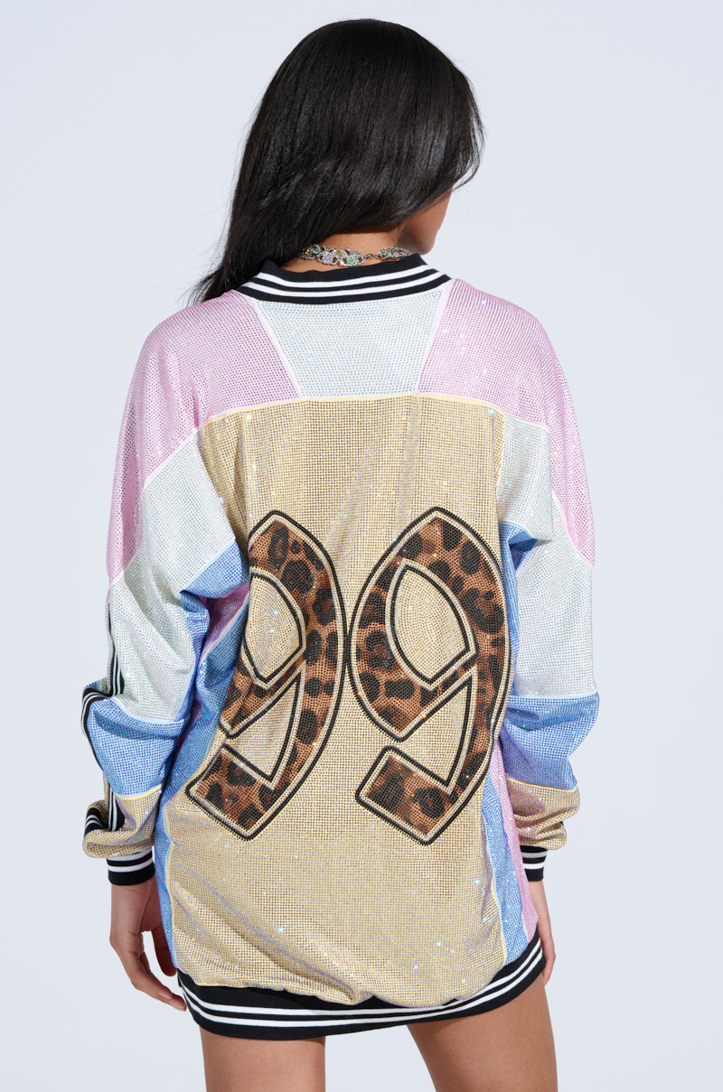 A person facing away from the camera wears the RYAN COLORBLOCK RHINESTONE JERSEY MINI DRESS IN PASTEL, a sparkly multicolored mini dress with black and white striped trim and a large leopard-print number "99" on the back.