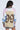 A person facing away from the camera wears the RYAN COLORBLOCK RHINESTONE JERSEY MINI DRESS IN PASTEL, a sparkly multicolored mini dress with black and white striped trim and a large leopard-print number 