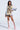 A woman poses confidently in the RYAN COLORBLOCK RHINESTONE JERSEY MINI DRESS IN PASTEL, styled with knee-high lace-up pink platform boots and a necklace, set against a plain background.