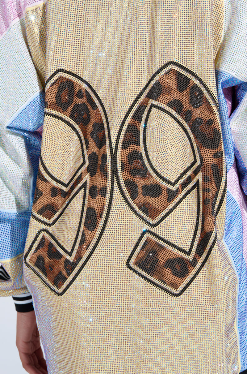 A close-up of the RYAN COLORBLOCK RHINESTONE JERSEY MINI DRESS IN PASTEL shows a sparkling gold mesh back with bold leopard-print 99 and blue-white colorblock sleeves, echoing jersey style with rhinestone flair.