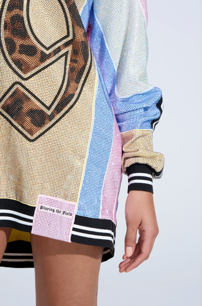 The visible lower torso and hand show off the RYAN Colorblock Rhinestone Jersey Mini Dress in Pastel, featuring colorful mesh, black and white striped cuffs and hem, a bold leopard print number graphic, and a pink "Playing the Field" patch.