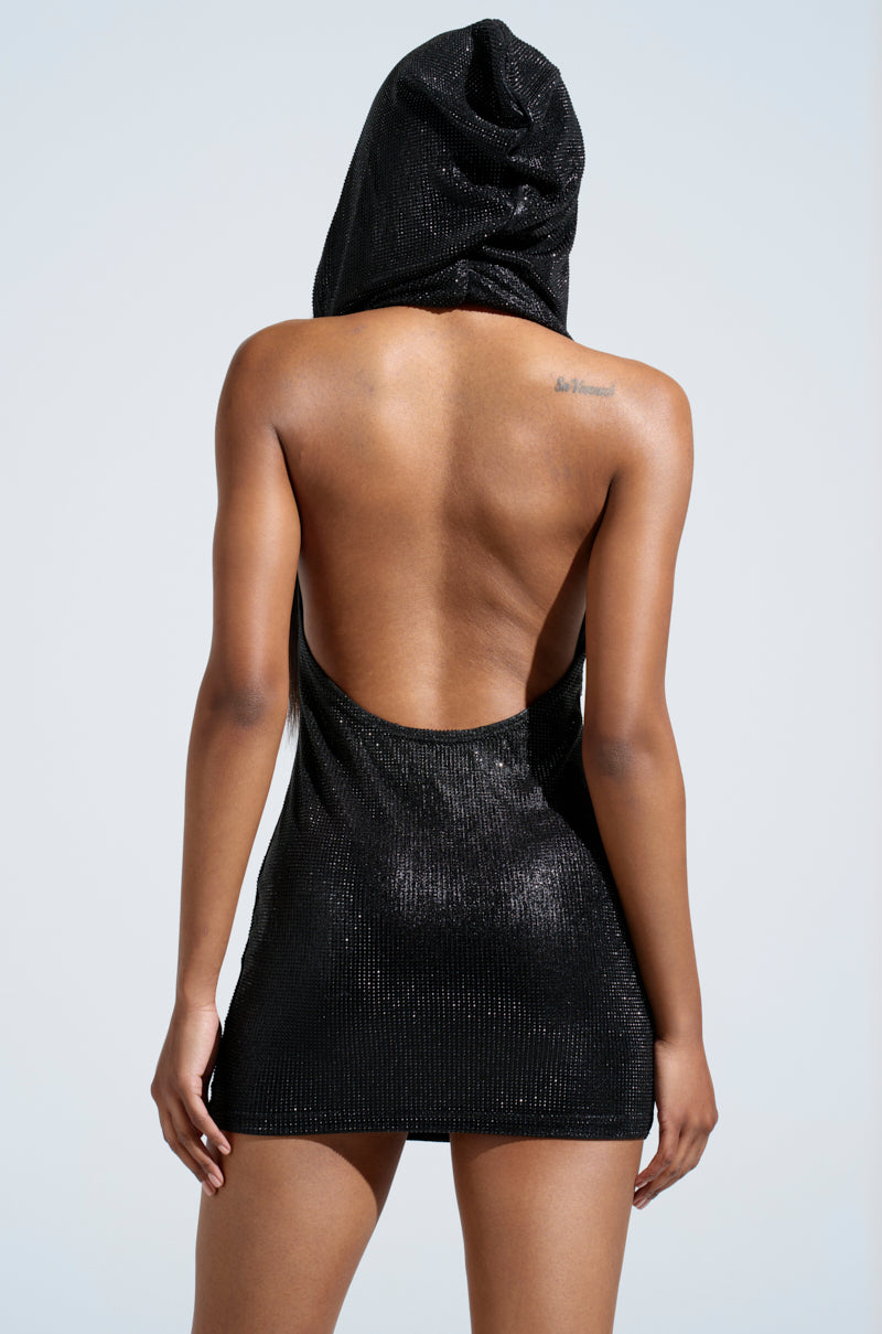 A person faces away, revealing their bare back and a small upper right shoulder tattoo, while wearing the BADDIE BEHAVIOR HOODED MINI DRESS—a shimmery black metallic mini dress with rhinestone embellishments.