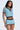 A woman wears the REBEL COLLARED TOP with high-waisted shorts in a colorful blue, brown, and white zigzag pattern, featuring 