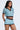 A woman wears the REBEL COLLARED TOP, featuring a blue, white, and brown zigzag pattern, paired with matching shorts. She stands with one hand on her hip, looking to the side.