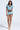 A woman stands confidently in the REBEL COLLARED TOP with matching high-waisted zigzag shorts, her long hair flowing as she completes the look with platform sandals.