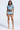 A woman faces forward wearing the REBEL COLLARED TOP, a colorful zigzag short-sleeve crop top with black trim and high-waisted shorts, paired with beige platform heels for a bold, standout look.