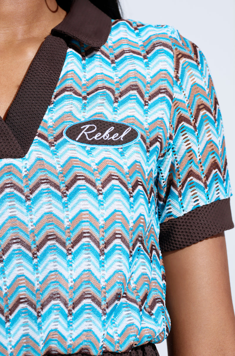 Close-up of the REBEL COLLARED TOP, showcasing its vibrant zigzag pattern with brown collar and cuffs. An oval "Rebel" embroidered patch adds a unique touch. Only the shoulder and part of the neck are visible.