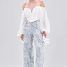 A woman stands against a plain light background wearing a white off-the-shoulder sheer blouse, the BOOKED N BUSY JACQUARD TROUSER in a high-rise fit, white heeled sandals, and holding a small white purse.