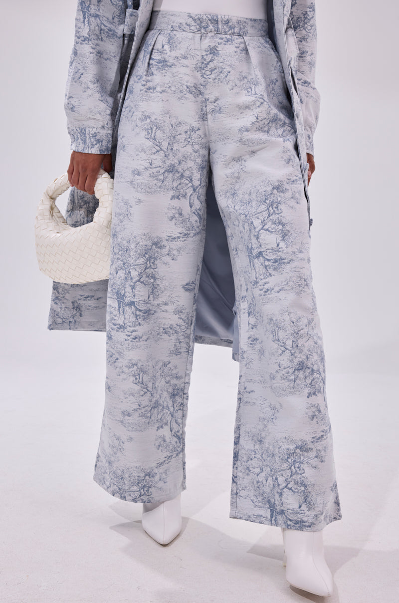 A person wears the BOOKED N BUSY JACQUARD TROUSER with a matching long coat and white pointed-toe boots, holding a small white woven handbag against a plain white background.