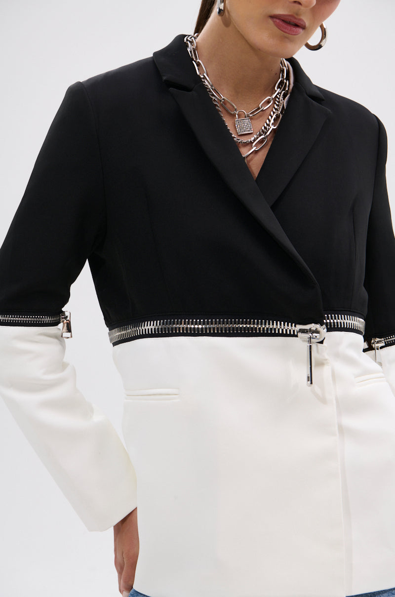 A woman styles the DON'T TRIP ZIPPER BLAZER—a dual-tone piece in black and white—with layered silver chains and hoop earrings for a standout look.