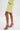 A person stands on a white background in a pastel outfit, wearing the SMELL THE FLOWERS BERMUDA SHORT with a matching jacket and gold strappy high-heeled sandals wrapped around the ankles, hands tucked in pockets.