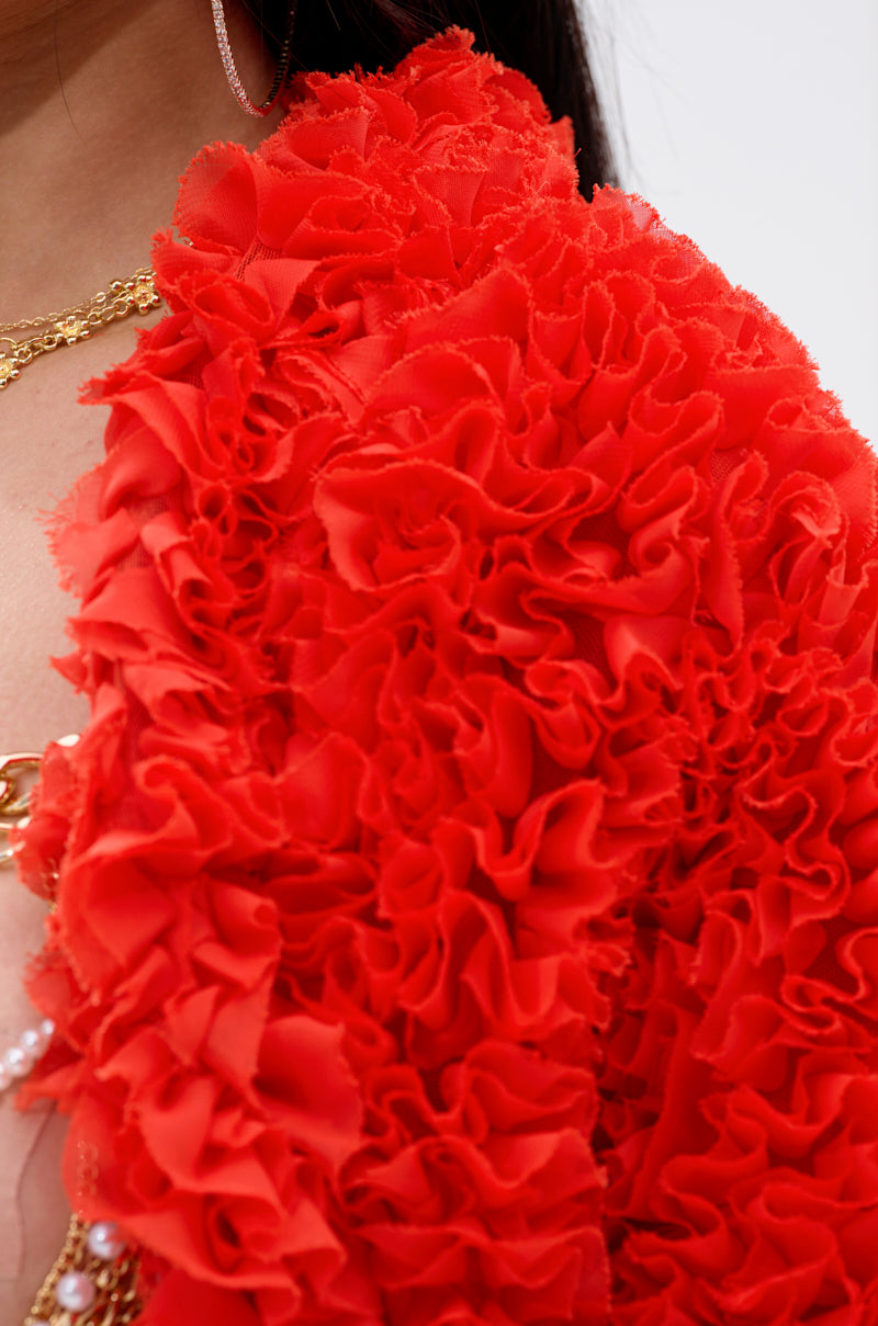 Close-up of a cropped silhouette wearing the FIRED UP CHIFFON SHRUG with vibrant red ruffles, gold chain jewelry, and hoop earrings. The exaggerated sleeves add volume and texture, partially revealing the wearer’s face and shoulder.