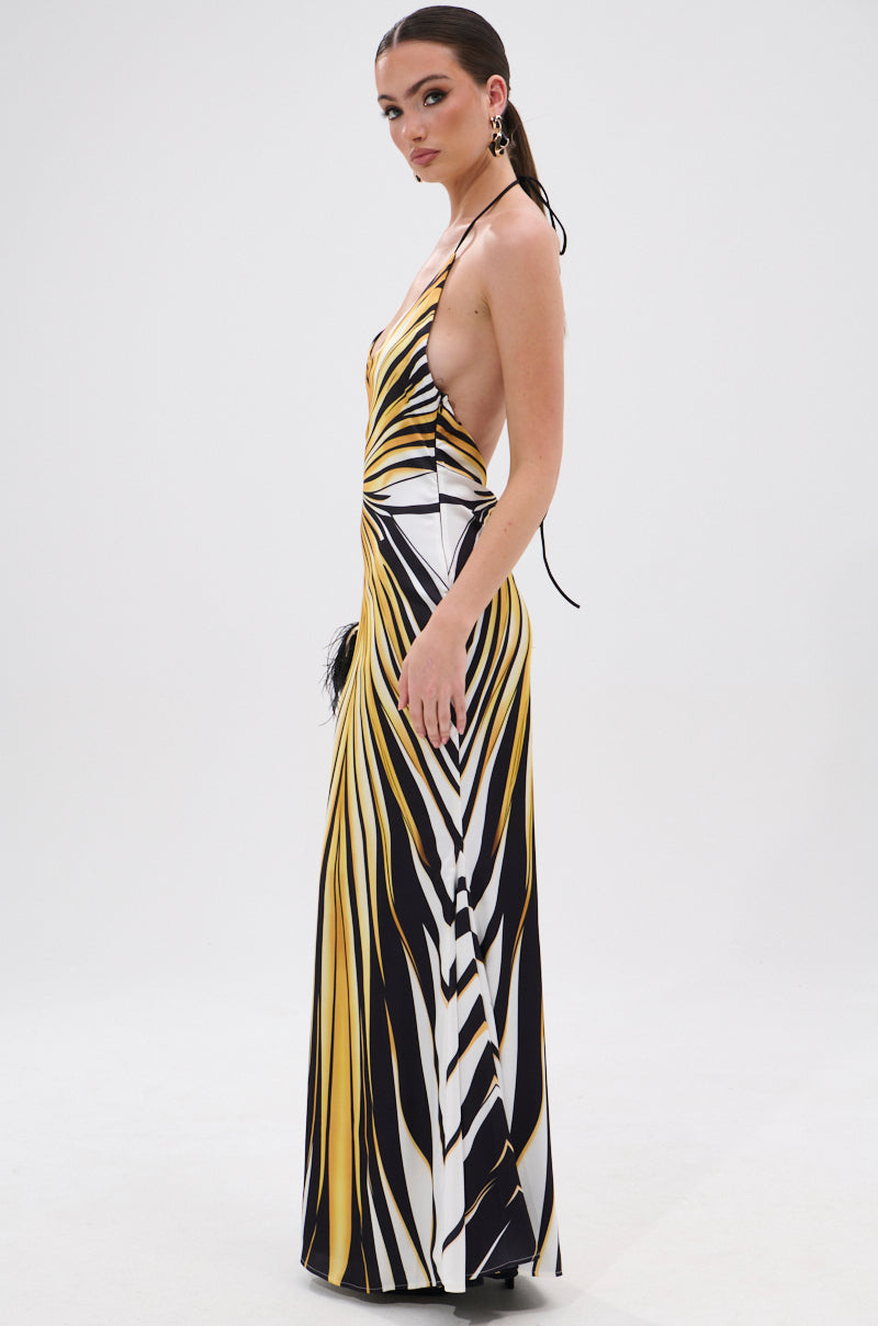 A woman stands in profile wearing the COVER STAR PRINTED SATIN MIDI DRESS, featuring a bold geometric pattern in yellow, black, and white, side cutouts, a low back, and a curve-flattering mermaid silhouette against a plain white background.