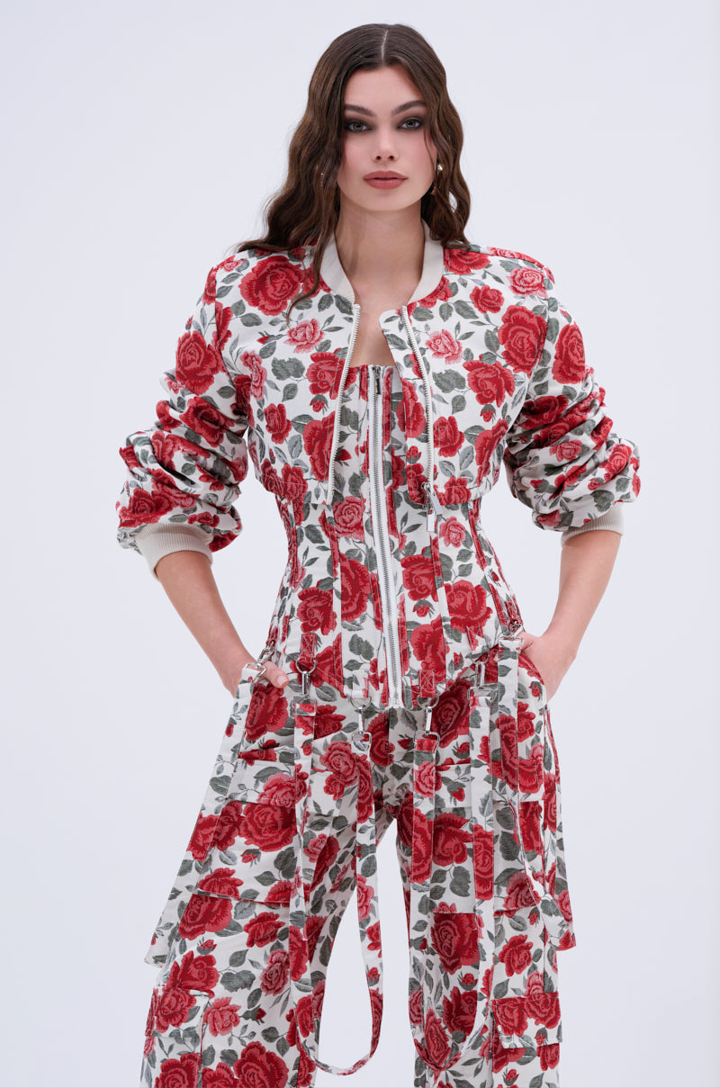 A woman stands with her hands in her pockets against a plain light background, showcasing effortless streetwear style in the FULL OF ROSES CROPPED BOMBER and matching rose print wide-leg pants.