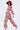A woman walks in streetwear fashion, wearing the FULL OF ROSES CROPPED BOMBER and matching wide-leg pants in a red and pink rose print, paired with a large black hat topped with red flowers and white heeled sandals.