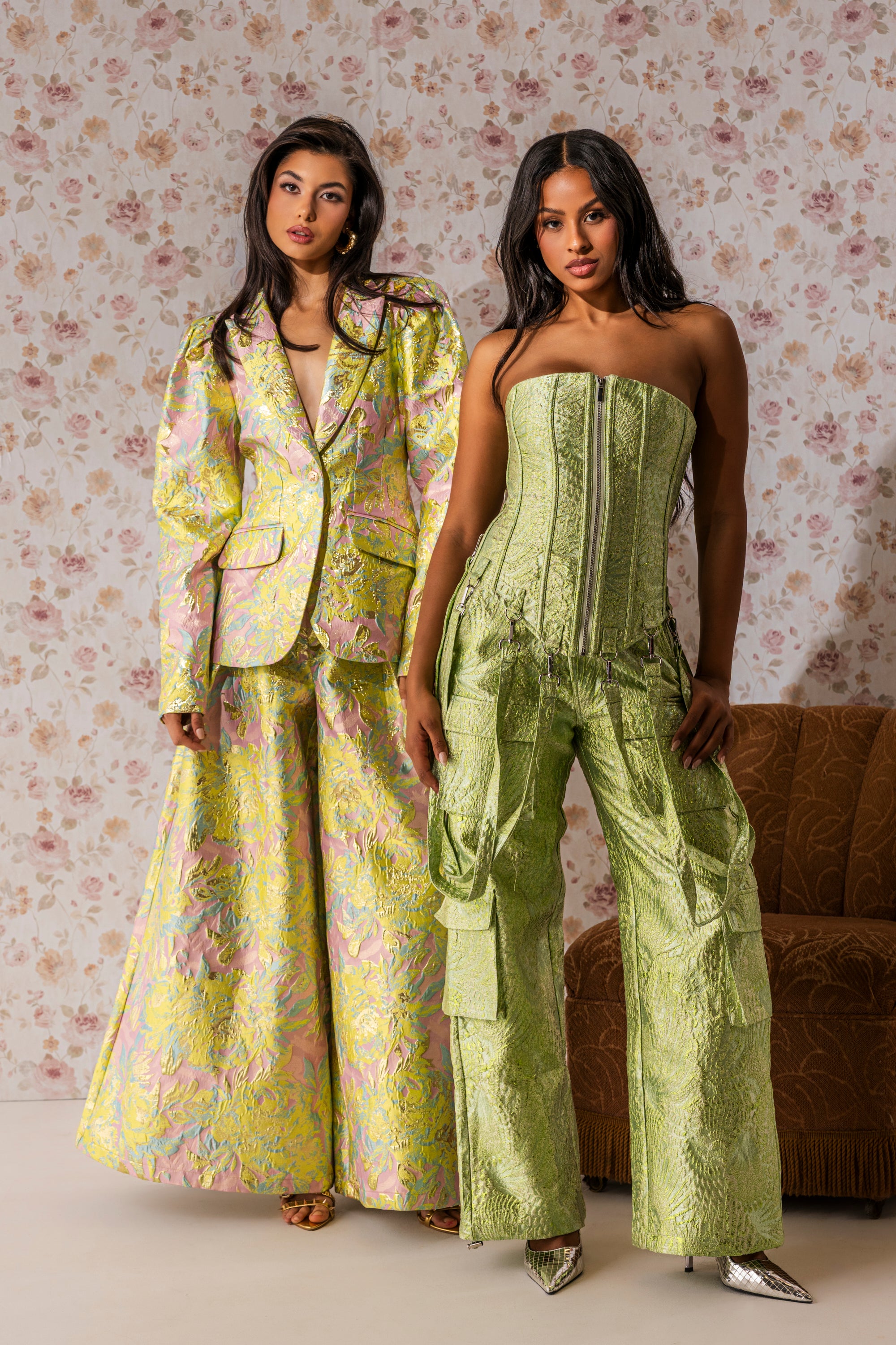 Two women pose against floral wallpaper. One wears a shiny suit; the other pairs pointed heels with a strapless green corset top and ENVY ME BROCADE PANT cargo pants for a bold, fashion-forward style. 1