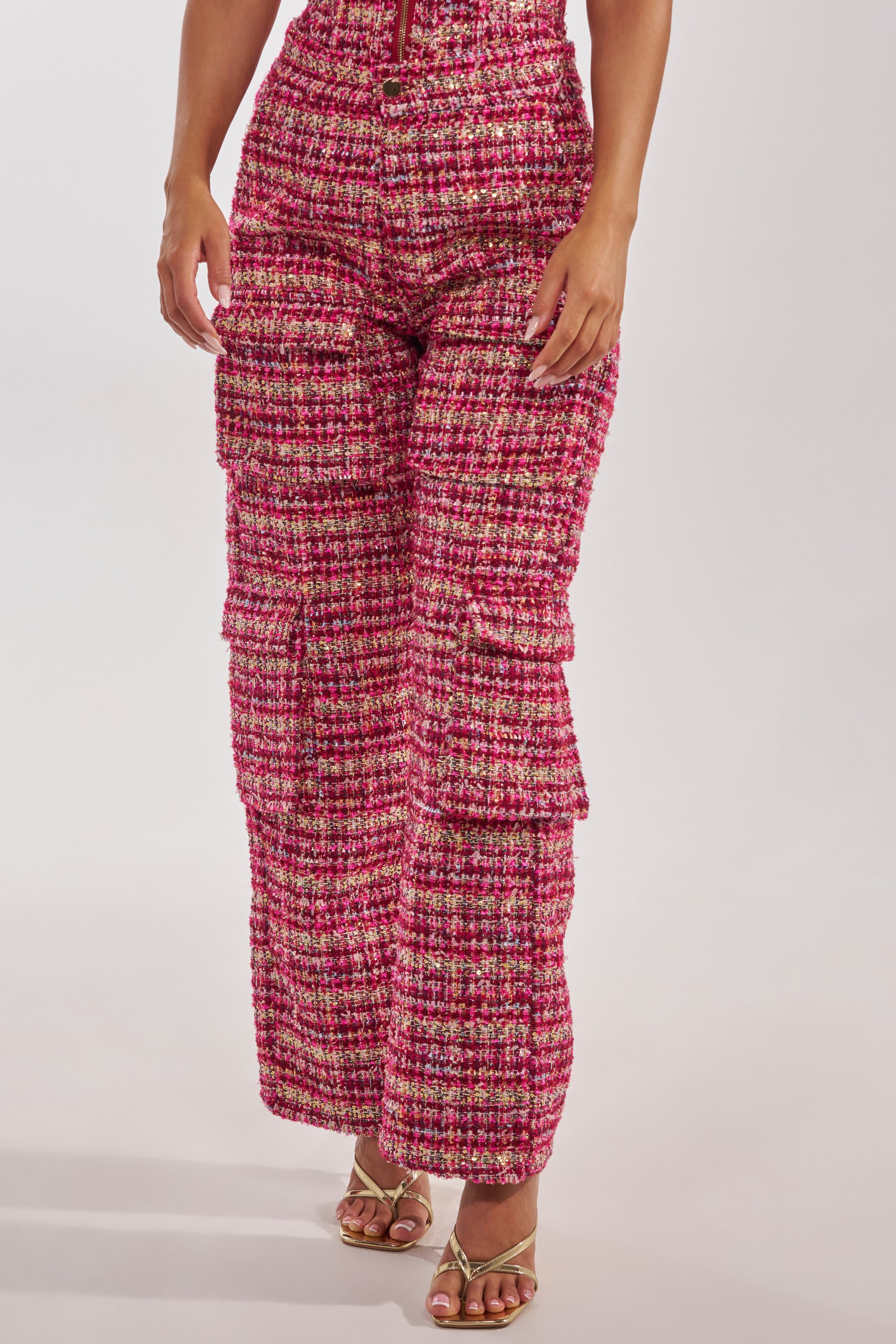 Someone stands against a plain background wearing the ITS TIME TWEED TROUSER—high-rise, wide-leg pants with multiple cargo pockets and gold buttons—paired with strappy gold heeled sandals. 1