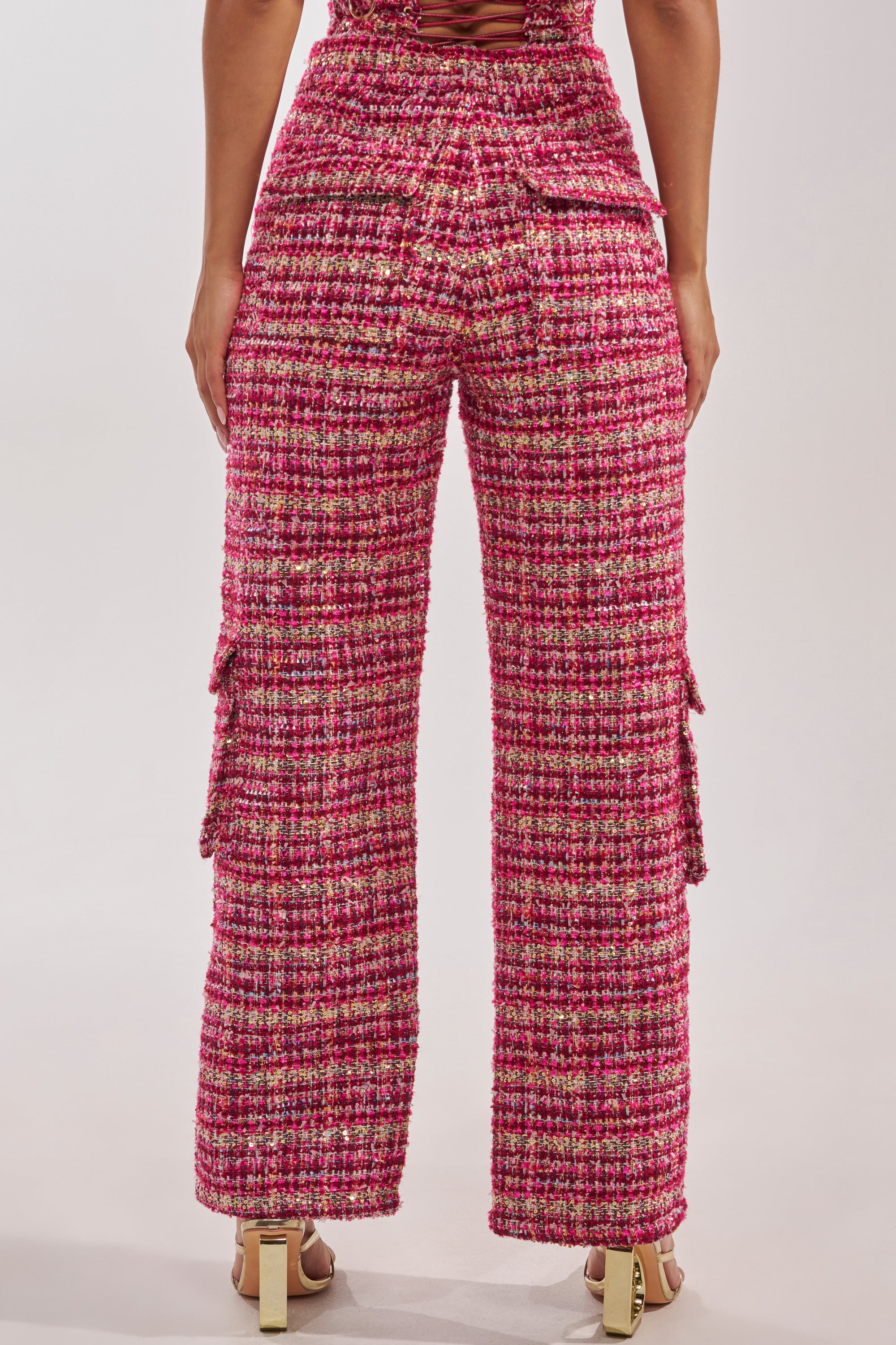 A person is seen from behind wearing the ITS TIME TWEED TROUSER—high-rise, pink and red tweed with a straight-leg fit and side pockets—paired with beige heeled sandals against a plain light background. 3