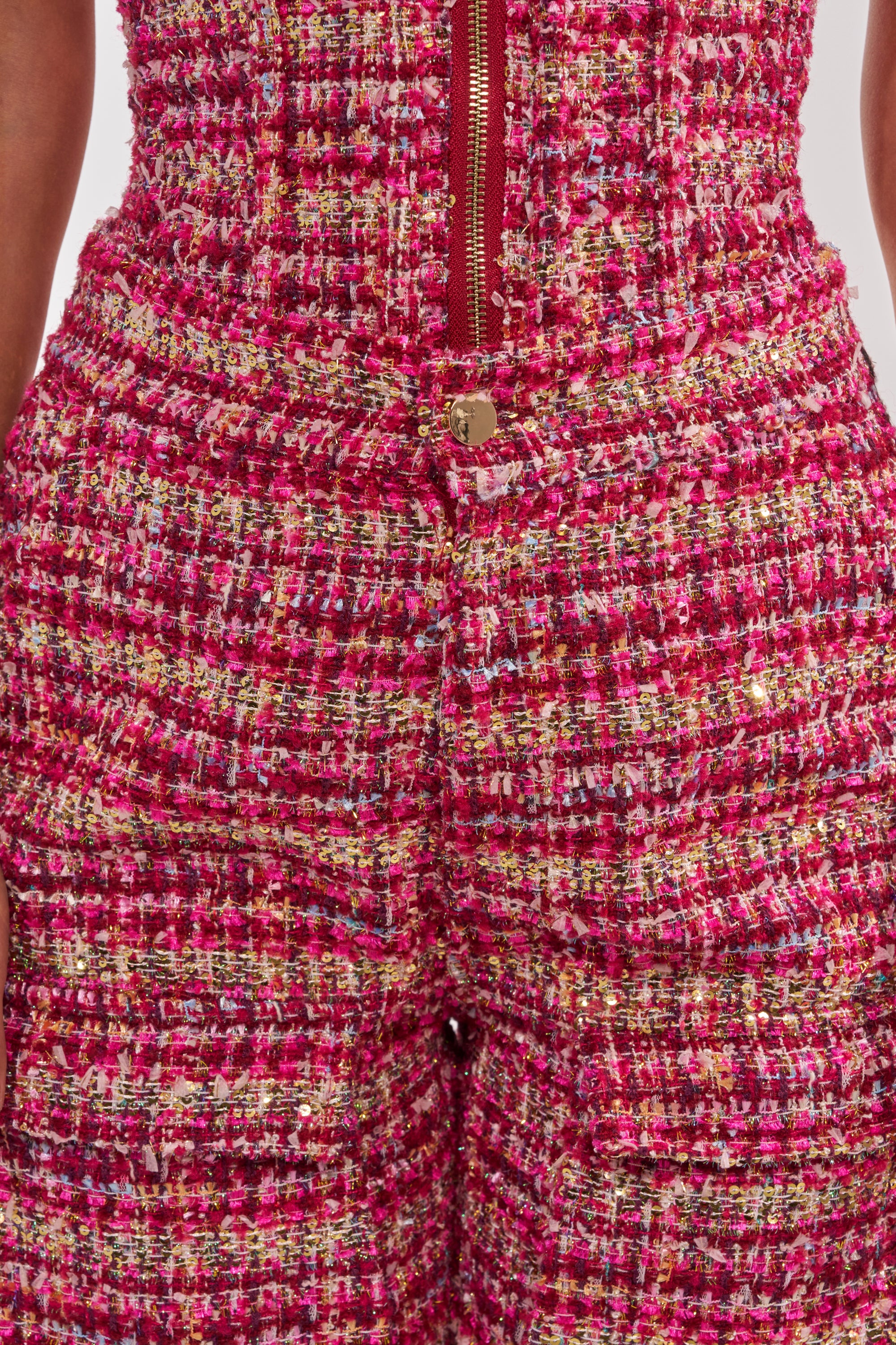 Close-up of a person wearing ITS TIME TWEED TROUSER, featuring a high-rise waist, multicolored pink, red, yellow, and white textured tweed fabric with metallic threads, front zipper, and button. 7