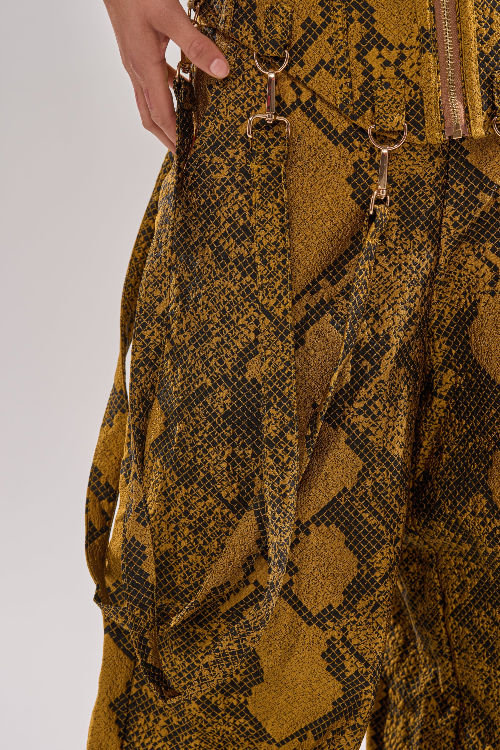 Close-up of a person wearing the SEXY LITTLE THANG SNAKE CORSET in yellow and black snakeskin print with gold hardware details, lace-up panels, and straps, one hand resting near the waistband.