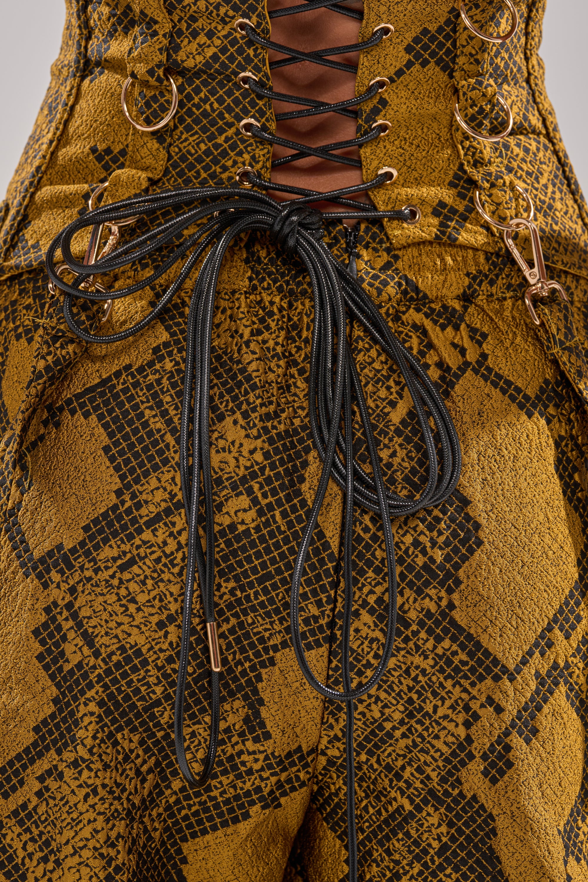Close-up of the SEXY LITTLE THANG SNAKE CORSET, showcasing a gold and black snakeskin pattern, black lace-up bow, and gold ring accents—a bold corset with snake-inspired panel detail.