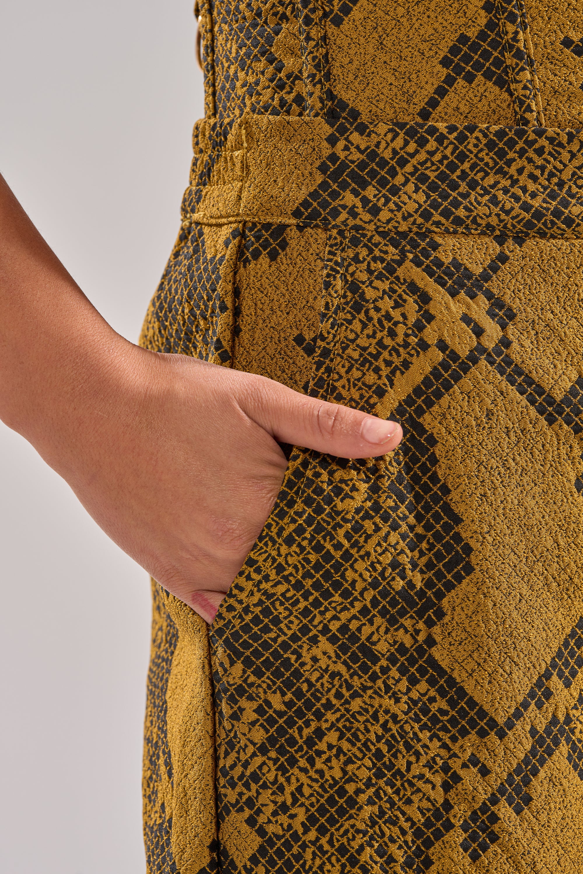 A close-up of a person’s hand in the pocket of SEXY LITTLE THANG SNAKE TROUSER, featuring high-rise wide-leg pants with a bold black snakeskin print, against a plain light background.