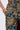 A close-up of a person wearing the SURRENDER FLORAL TROUSER in shimmering brocade, with one hand in their pocket and gold bangles on their wrist.