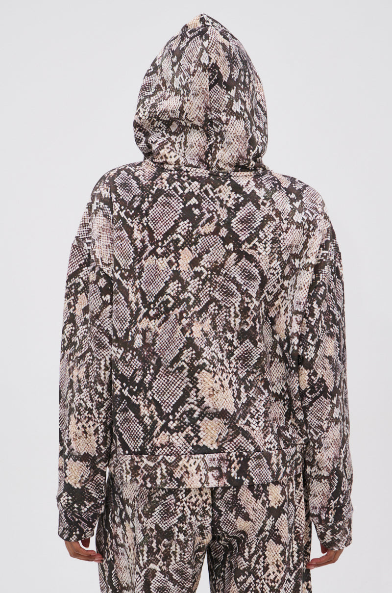 A person stands with their back to the camera against a white background, wearing an oversized PYTHON HOODED SWEATSHIRT and matching snakeskin-patterned pants that highlight the outfit’s bold style. 6