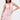 A woman with straight dark hair and tattoos poses confidently against a white background in the ALL EYES ON ME MINI DRESS IN PINK, featuring a ruched design and deep V neckline.